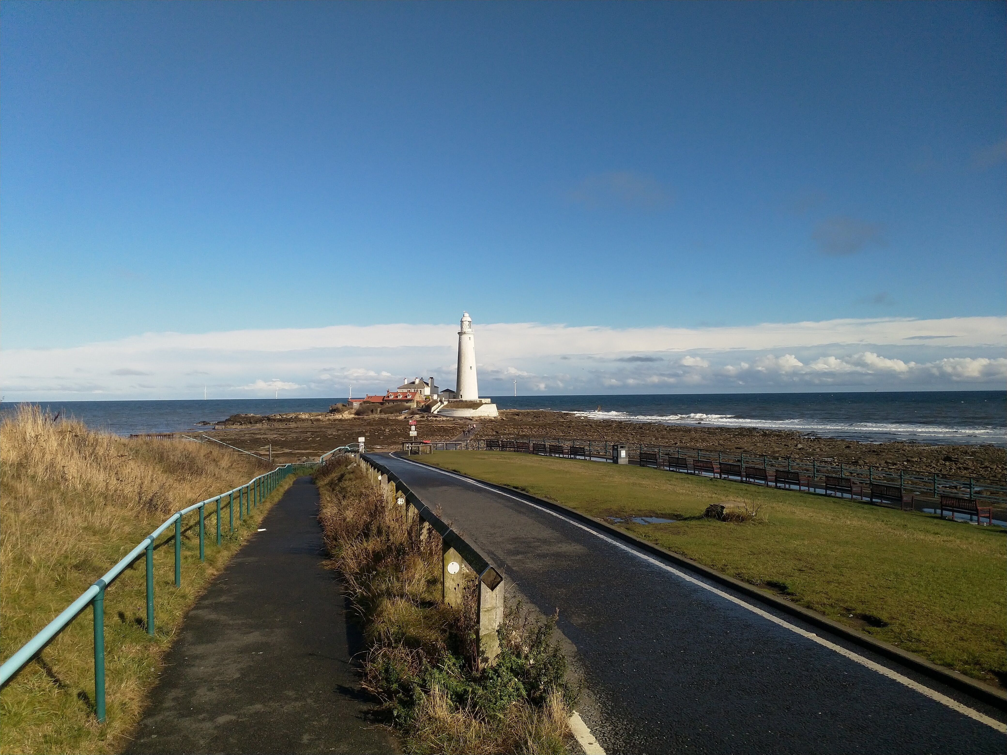 A beach crowded with people. There is a lighthouse in the far distance